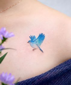 a small blue bird tattoo on the back of a woman's left shoulder and chest