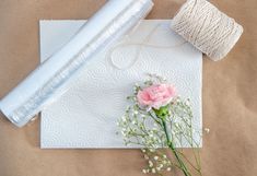 a roll of twine next to a pink flower and spool of thread on top of a piece of paper