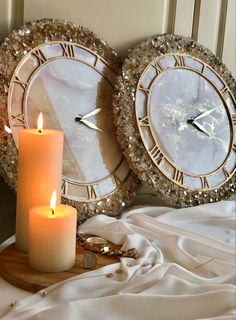 two clocks sitting on top of a bed next to a candle