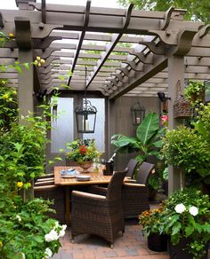 an outdoor dining area with potted plants on the table and wicker chairs around it