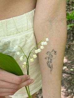 a woman holding a plant with lily of the valley tattoo on her left arm and wrist