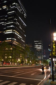 an empty city street at night with tall buildings in the background and people walking on the sidewalk