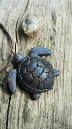 a small turtle is sitting on a wooden surface next to a rock and a leather cord