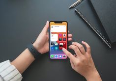 a person holding an iphone in their hand on top of a black table next to a pen and notebook