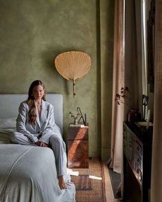 a woman sitting on top of a bed next to a window in a green room