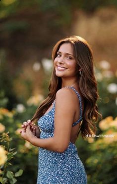 a beautiful young woman in a blue dress posing for the camera with roses behind her