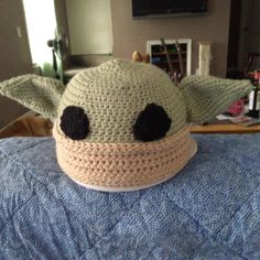 a crocheted baby yoda hat sitting on top of a blue bedspread