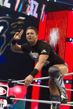 a man standing on top of a wrestling ring holding his hand up in the air