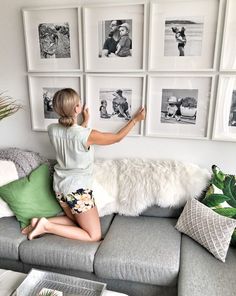 a woman sitting on top of a gray couch in front of pictures hanging on the wall