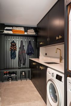 a washer, dryer and cabinets in a small room with clothes hanging on the wall