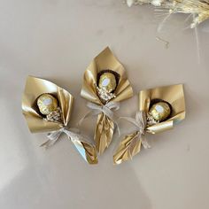 three wrapped chocolates in gold wrappers on a table