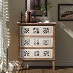 a white dresser with black and white designs on the drawers in front of a window