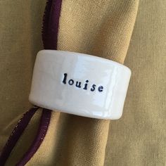 a white ring with the word louise on it sitting on top of a cloth