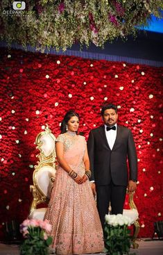 a man and woman standing next to each other in front of a red flower wall