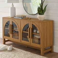 a wooden sideboard with glass doors and baskets on the bottom, in front of a white wall