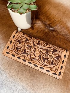 a brown leather wallet sitting on top of a fur covered floor next to a potted plant