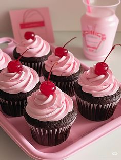 cupcakes with pink frosting and cherries on a tray next to a drink