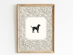 a black dog standing in front of a white wall with leaves on it's frame