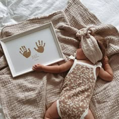 a baby laying on top of a bed next to a framed print with two hand prints