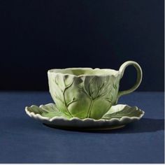 a green tea cup and saucer on a blue surface with the image of leaves painted on it