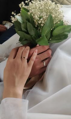 a person holding flowers in their hands on a white cloth covered bed with other people