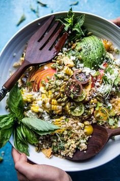 someone holding a white bowl filled with vegetables and rice on top of a blue table