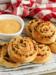 several rolls on a white plate with dipping sauce in the bowl next to it and two red checkered napkins