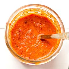 a glass jar filled with red sauce on top of a white countertop next to a wooden spoon