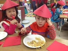 two children wearing party hats eating pasta at a table with red napkins on it