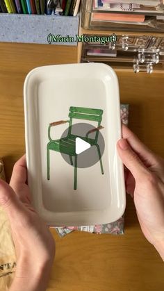 two hands holding a white tray with a green chair drawn on the front and side