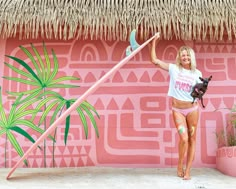 a woman holding a surfboard in front of a pink wall with palm trees on it