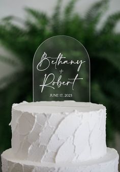 a white wedding cake with an acrylic topper