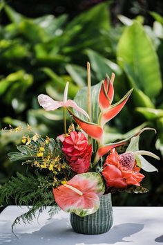 a vase filled with flowers on top of a white table next to green leaves and plants