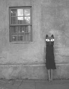 a woman standing in front of a building with a cat mask on it's head