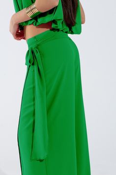 Introducing our Wide Green Pants Overlay Skirt, a stunning and versatile piece perfect for adding a touch of elegance to your party attire. This maxi-length overlay skirt features wide legs and a relaxed fit, providing both comfort and sophistication for any occasion.  Crafted from lightweight chiffon fabric, this overlay skirt drapes beautifully and flows with every movement. The knot detail at the side adds a chic and stylish touch, while the zip side closure ensures easy wear.  Perfect for parties or special events, this skirt can be paired with a variety of tops to create different looks. Made from 100% polyester with a polyester lining, it is durable and easy to care for, making it a practical choice for your wardrobe.  Our model is wearing size S, but the S-M-L sizing corresponds to Green Wide Leg Pants For Formal Summer Events, Green Wide Leg Pants For Summer Formal, Green Wide Leg Pants For Evening, Elegant Wrap Flowy Skirt, Elegant Wide Leg Pants With Tie Waist For Spring, Elegant Spring Wide Leg Pants With Tie Waist, Elegant Lined Skirt For Brunch, High Waist Green Maxi Skirt For Party, Elegant Summer Skirt With Tie Waist