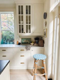 a kitchen with white cabinets and blue stools next to the counter top in front of an open window