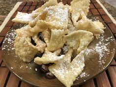 a plate filled with pasta and olives covered in powdered sugar on top of a wooden table