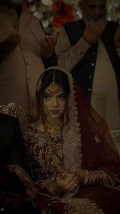 a woman in a red and gold bridal outfit sitting on a couch with other people