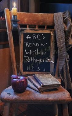 an apple, book and candle sit on a wooden chair in front of a chalkboard