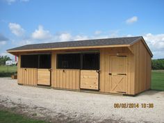 a horse barn with two stalls and one stall on gravel road next to grassy field