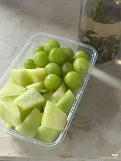 a plastic container filled with grapes and green apples