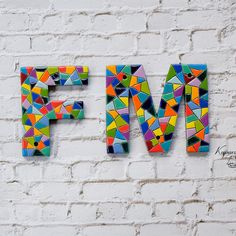 the letters f and m are made out of colorful mosaic tiles on a white brick wall