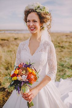 a woman in a white dress holding a bouquet and smiling at the camera while standing in a field