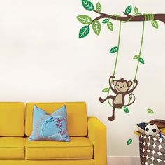 a living room with a yellow couch and monkey on the tree branch wall decal