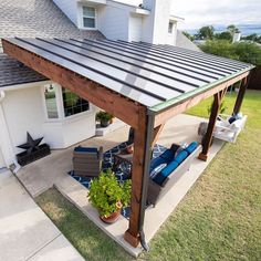 a covered patio with furniture and plants on the side walk in front of a house