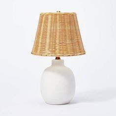 a white table lamp with a wicker shade on the base and a light bulb