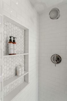 a white tiled shower with shelves holding soap and shampoos on the wall next to it