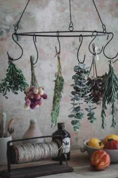 flowers and herbs hanging from hooks in a kitchen with other fruits and vegetables on the counter