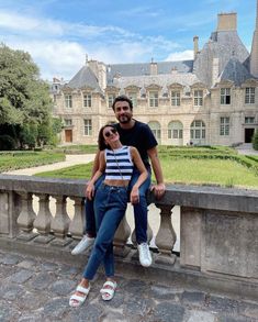 a man and woman are sitting on a stone wall in front of a large building