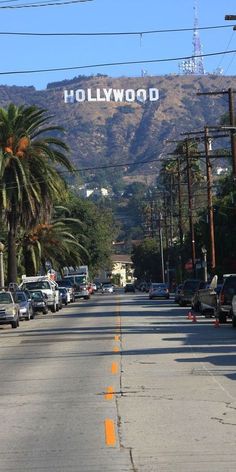 cars parked on the side of a road with hollywood sign in the background and palm trees lining the street